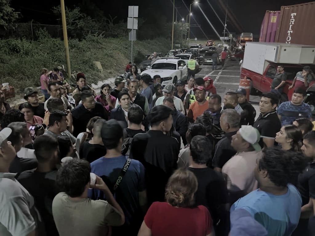 De noche, Salvador J. Vazquez Villa dialoga con un grupo numeroso de personas sobre la autopista, con vehículos detenidos al fondo.