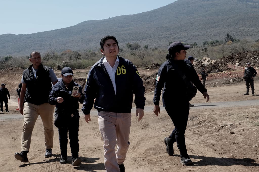 Salvador J. Vazquez Villa walks across a highway construction site alongside security personnel, with the mountains behind.